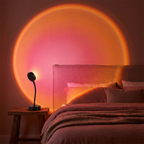Sunset projection lamp casting a rose-pink sun halo on a cozy bedroom wall