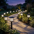 Row of square solar path lights glowing warm white along a garden walkway at dusk