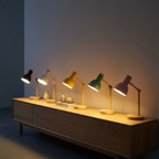 Row of five Nordic bedside lamps in black, white, yellow, green, and pink glowing warm on a console, showing all color options