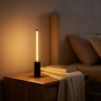 Slim vertical bar ambience lamp glowing softly warm on a calm bedside nightstand at night