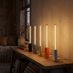 Row of five slim bar ambience lamps in black, dark gray, gold, orange, and silver glowing warm on a console, showing all finishes