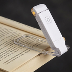 AuraLights clip-on book light, white body clipped to an open book, clean studio lighting